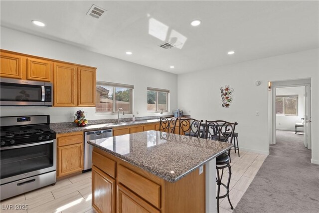 kitchen featuring visible vents, a kitchen island, appliances with stainless steel finishes, a sink, and a kitchen breakfast bar