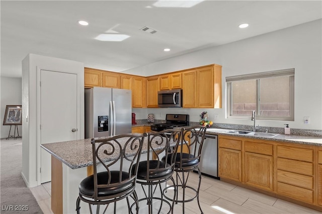 kitchen with visible vents, a kitchen bar, a kitchen island, appliances with stainless steel finishes, and a sink