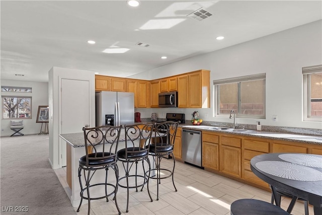 kitchen with a kitchen breakfast bar, a kitchen island, a sink, visible vents, and appliances with stainless steel finishes