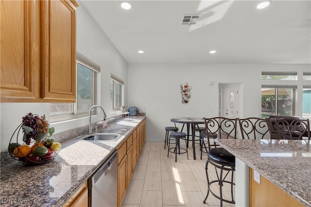 kitchen featuring a breakfast bar area, a sink, light stone counters, visible vents, and dishwasher