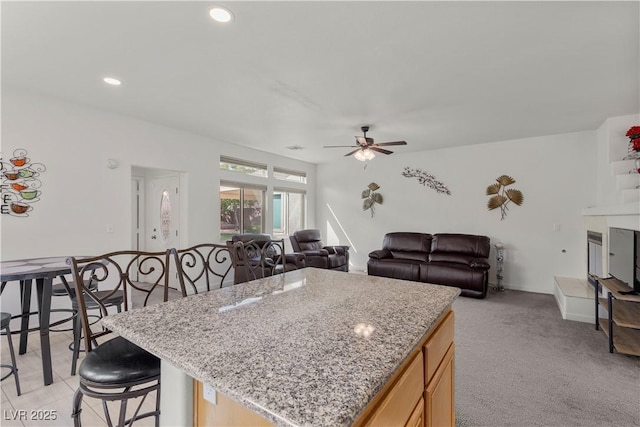 kitchen featuring light stone counters, a kitchen island, a kitchen bar, ceiling fan, and recessed lighting