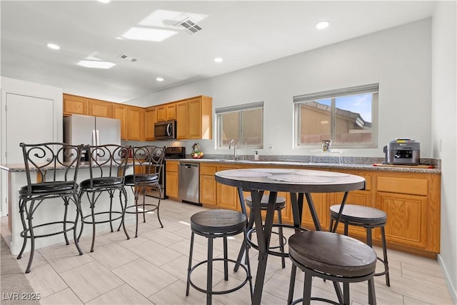 kitchen featuring a wealth of natural light, a sink, a breakfast bar, stainless steel appliances, and visible vents