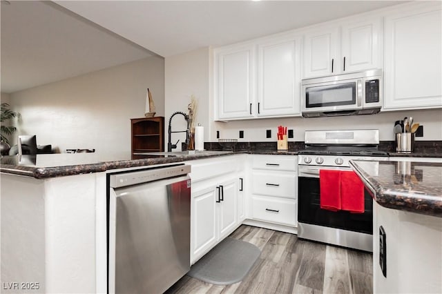 10091 Sand Key St, Las Vegas, NV 89178 - kitchen featuring appliances with stainless steel finishes, a peninsula, white cabinets, dark stone countertops, and light wood-style floors