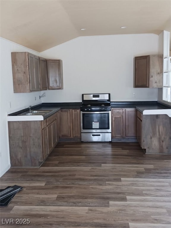 kitchen featuring dark wood-style flooring, dark countertops, stainless steel range with gas cooktop, a sink, and vaulted ceiling