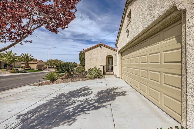 view of home's exterior with concrete driveway, a tiled roof, a gate, and stucco siding