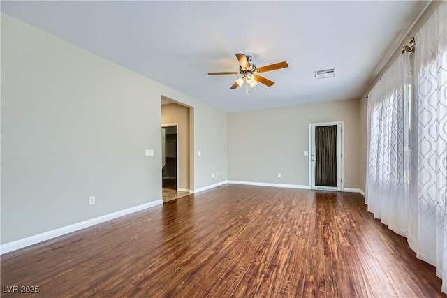 spare room with dark wood-type flooring, a ceiling fan, visible vents, and baseboards