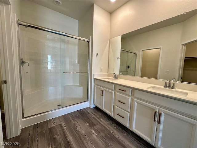 full bathroom featuring double vanity, a sink, a stall shower, and wood finished floors