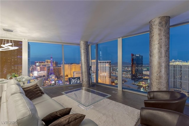 living area with a view of city lights, ornate columns, tile patterned floors, and a wall of windows