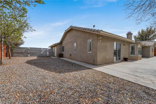 back of house featuring stucco siding, fence, a patio, a gate, and a chimney