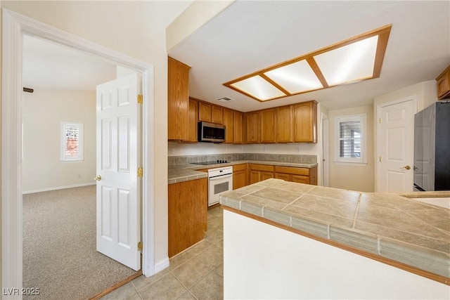 kitchen featuring tile counters, light carpet, appliances with stainless steel finishes, and a healthy amount of sunlight