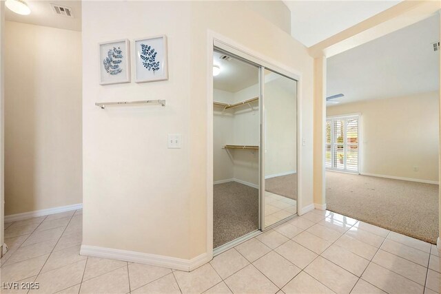 hallway featuring baseboards, visible vents, tile patterned floors, and carpet