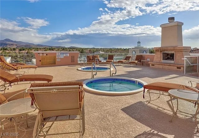 view of pool featuring a community hot tub, an outdoor fireplace, a swimming pool, a patio area, and a mountain view