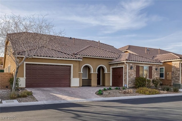 mediterranean / spanish house featuring stucco siding, fence, an attached garage, a tiled roof, and decorative driveway
