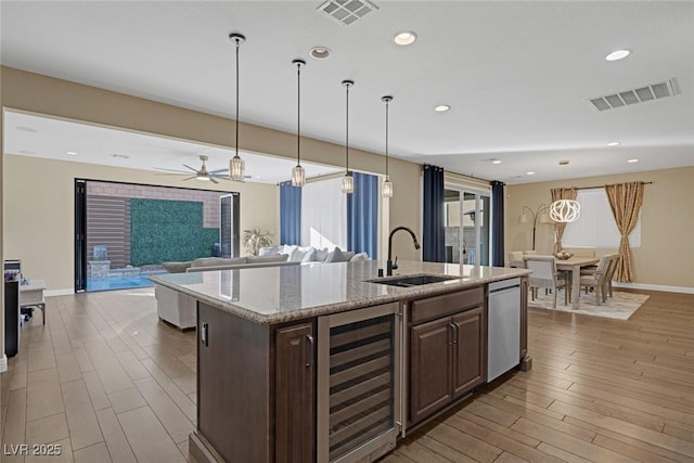 kitchen featuring stainless steel dishwasher, a sink, beverage cooler, visible vents, and wood finished floors