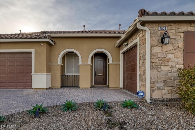 doorway to property with stone siding, driveway, an attached garage, a tile roof, and stucco siding