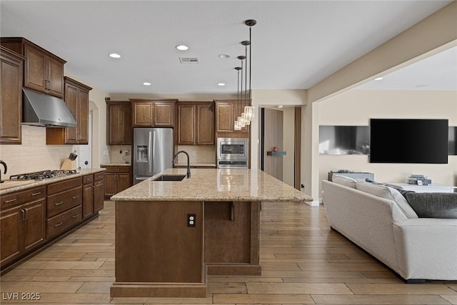 kitchen with a sink, appliances with stainless steel finishes, open floor plan, under cabinet range hood, and visible vents