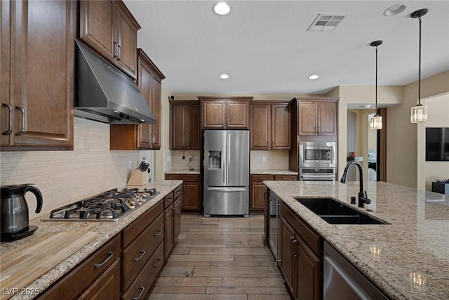 kitchen featuring stainless steel appliances, under cabinet range hood, a sink, visible vents, and wood finished floors