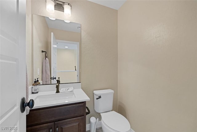 half bathroom with baseboards, toilet, and vanity