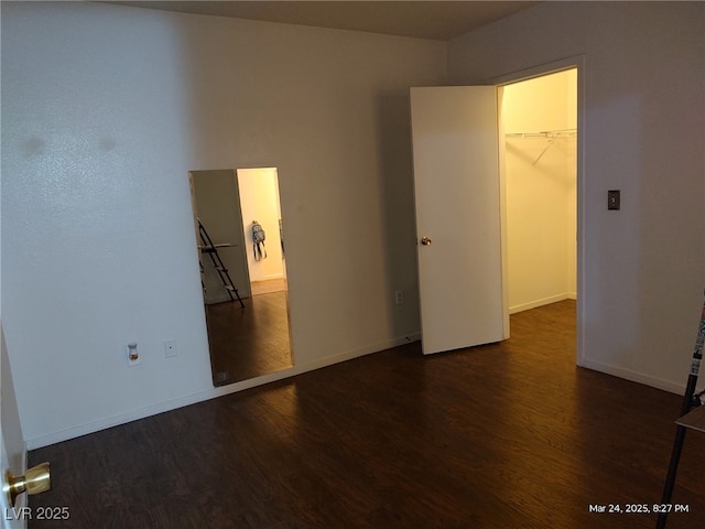 unfurnished bedroom with wood finished floors, a closet, baseboards, and a spacious closet
