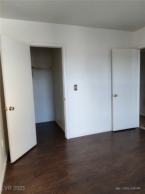 unfurnished bedroom with a spacious closet, a closet, baseboards, and dark wood finished floors