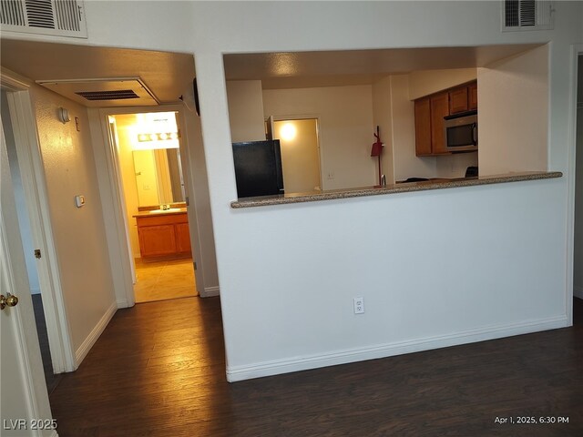 kitchen with stainless steel microwave, visible vents, baseboards, and dark wood-style floors