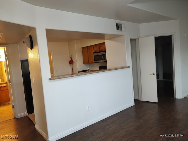 kitchen with brown cabinets, visible vents, stainless steel microwave, and dark wood-style flooring