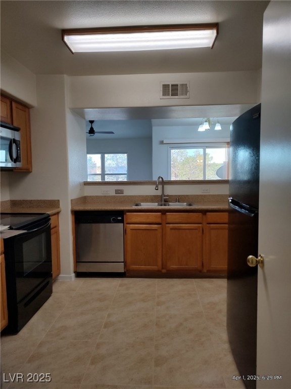 kitchen with brown cabinetry, visible vents, a sink, and black appliances