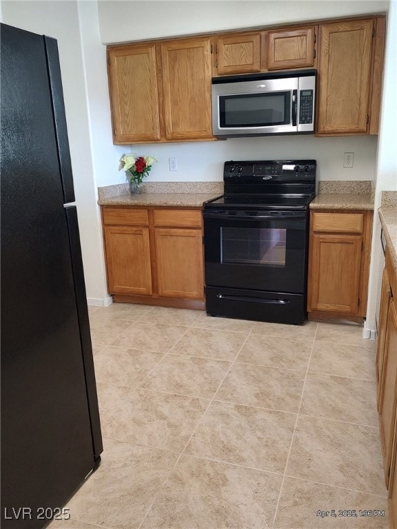 kitchen featuring brown cabinets, light countertops, black appliances, and light tile patterned floors