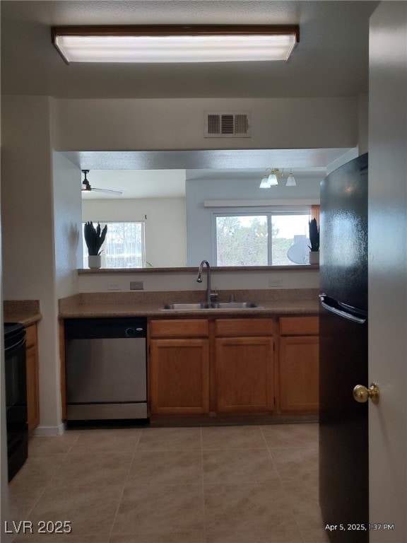 kitchen featuring dishwasher, freestanding refrigerator, visible vents, stove, and a sink