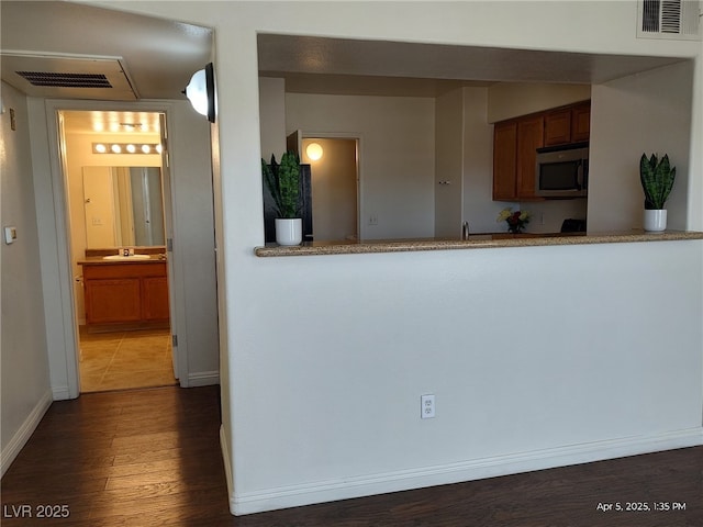 kitchen with visible vents, stainless steel microwave, brown cabinetry, and dark wood-style floors