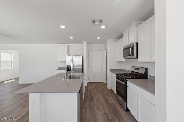 kitchen featuring visible vents, appliances with stainless steel finishes, a sink, an island with sink, and dark wood-style floors