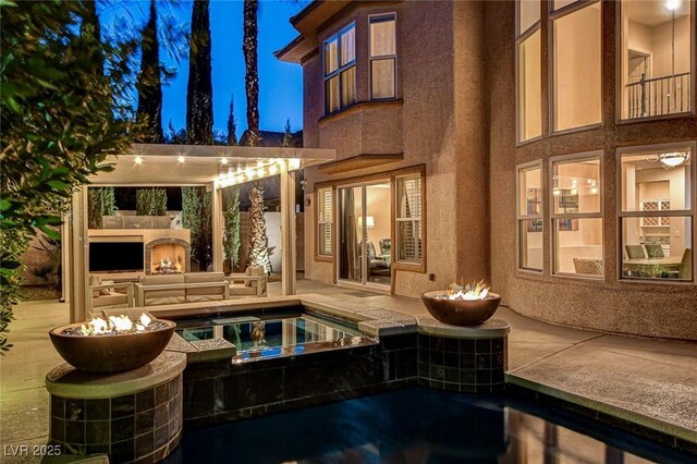 back of house featuring a warm lit fireplace, a patio area, and an in ground hot tub