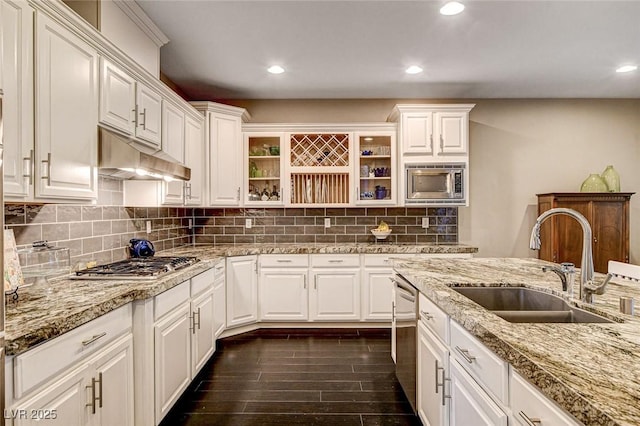 kitchen with decorative backsplash, under cabinet range hood, white cabinets, a sink, and stainless steel appliances