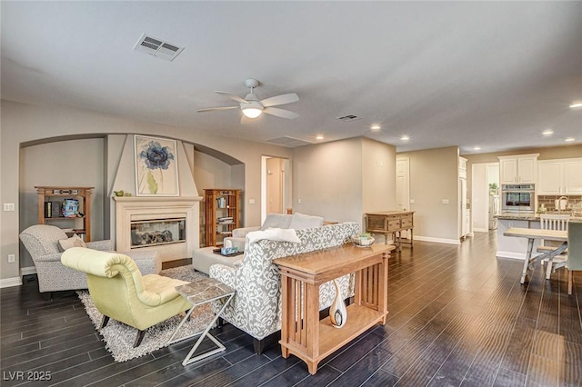 living room featuring dark wood-style flooring, arched walkways, ceiling fan, and visible vents