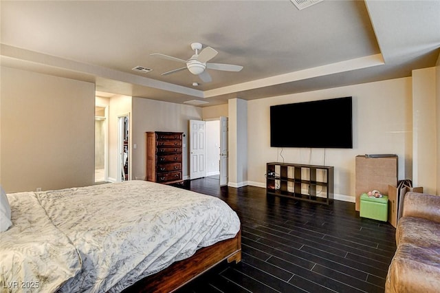bedroom with baseboards, visible vents, wood finished floors, and a raised ceiling