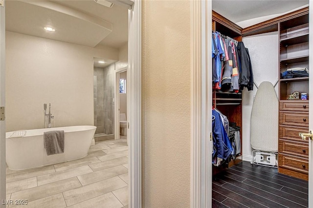 full bathroom featuring toilet, wood finish floors, a spacious closet, and a freestanding bath