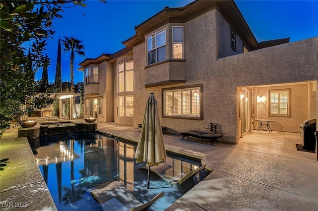 back of house at night featuring a patio area, stucco siding, and an outdoor pool