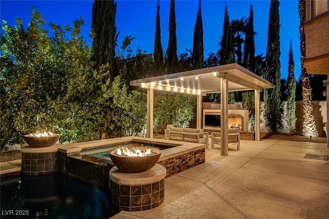 patio at twilight featuring a warm lit fireplace