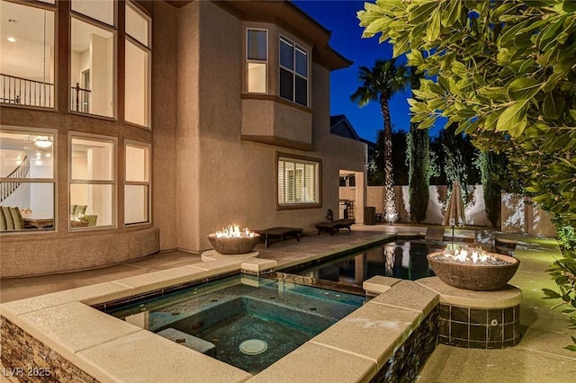 pool at twilight featuring fence, an in ground hot tub, and a patio area