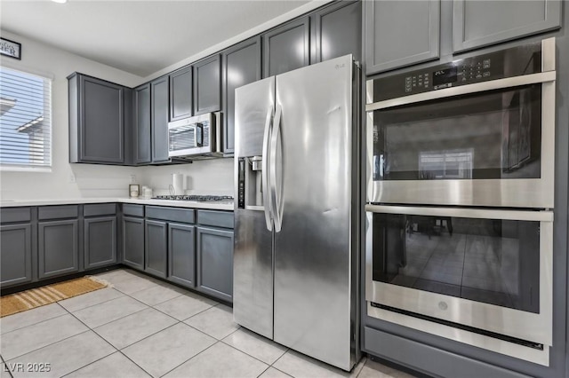 kitchen with gray cabinetry, appliances with stainless steel finishes, light tile patterned flooring, and light countertops