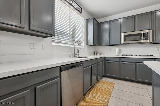 kitchen featuring gray cabinets, light tile patterned floors, a sink, and stainless steel appliances