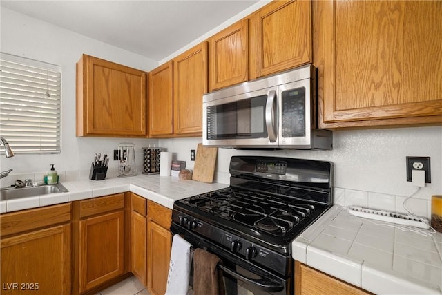 388 Coronado Dr, Henderson, NV 89015 - kitchen featuring black range with gas stovetop, stainless steel microwave, a sink, tile counters, and brown cabinetry