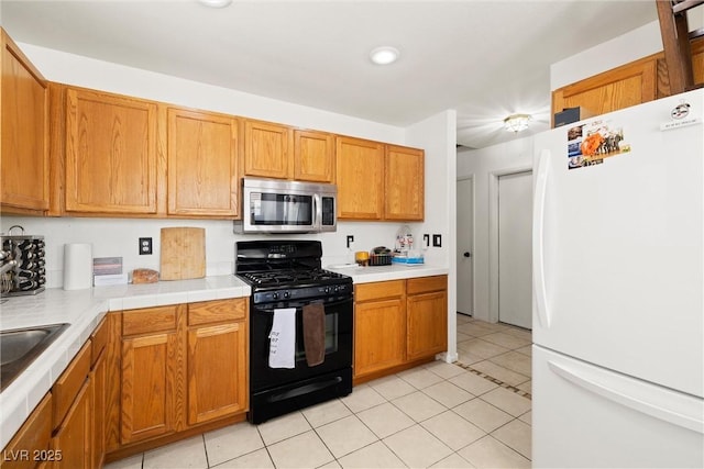 388 Coronado Dr, Henderson, NV 89015 - kitchen featuring freestanding refrigerator, stainless steel microwave, black gas stove, light tile patterned floors, and brown cabinetry