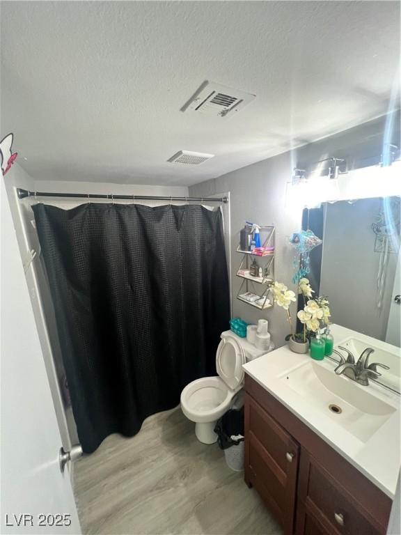 bathroom with wood finished floors, a textured ceiling, vanity, a shower with shower curtain, and toilet