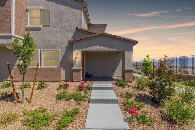entrance to property featuring fence and stucco siding