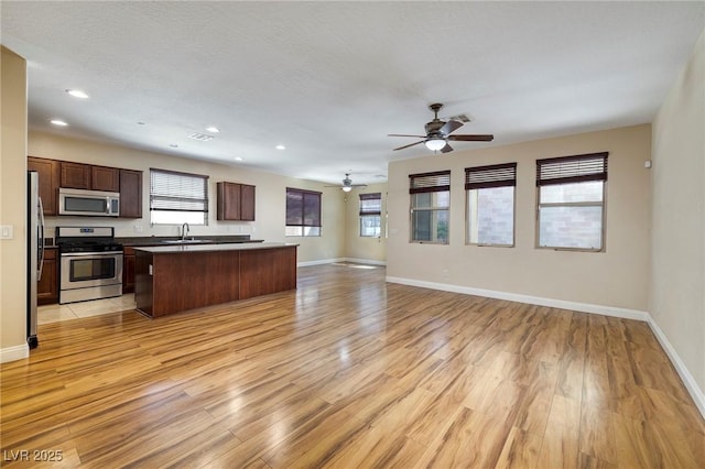 kitchen with baseboards, stainless steel appliances, open floor plan, and light wood-style flooring