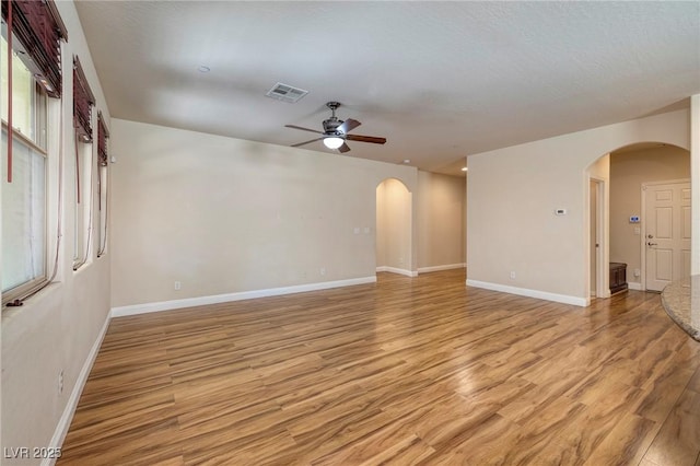 unfurnished room with arched walkways, ceiling fan, visible vents, and light wood-style flooring