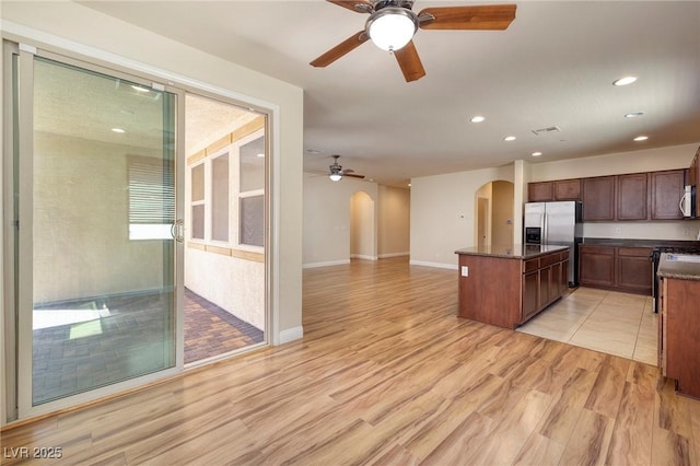 kitchen featuring visible vents, ceiling fan, a center island, stainless steel refrigerator with ice dispenser, and arched walkways