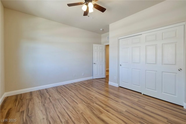 unfurnished bedroom with a closet, baseboards, a ceiling fan, light wood finished floors, and vaulted ceiling