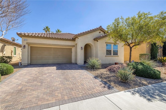 mediterranean / spanish house with stucco siding, an attached garage, a tile roof, and decorative driveway